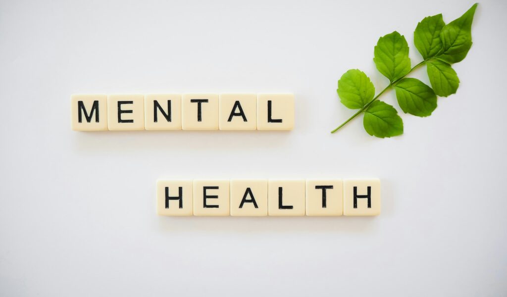 Tiles with the words “Mental Health” and green leaves represent well-being.